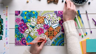 Aerial view of left handed woman coloring a design with gel pens.